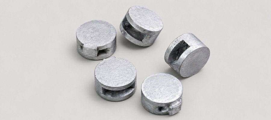 Five small silver round fishing weights with a side slot scattered on a light gray surface, on a pale background